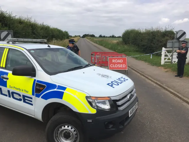 A police vehicle, with police officers, on a road in front of a sign saying road closed