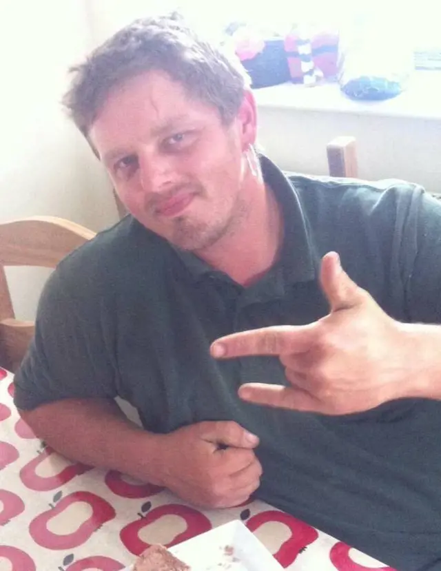 Stuart Dewing in dark polo shirt, sitting a table with apple-print covering