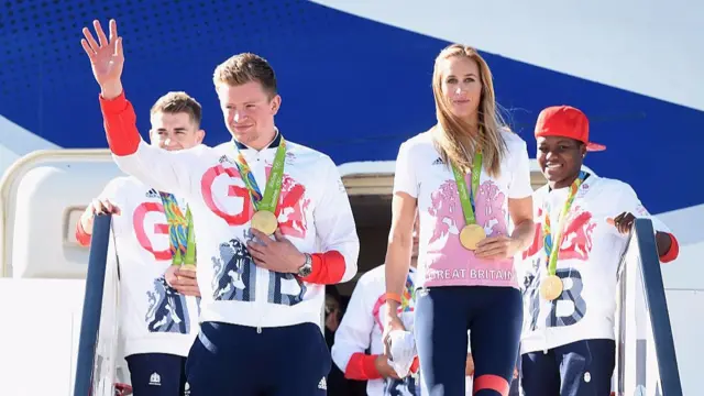 Adam Peaty waving to people from steps of the Team GB plane