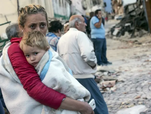 A woman holds a child as they stand in the street following the quake in Amatrice