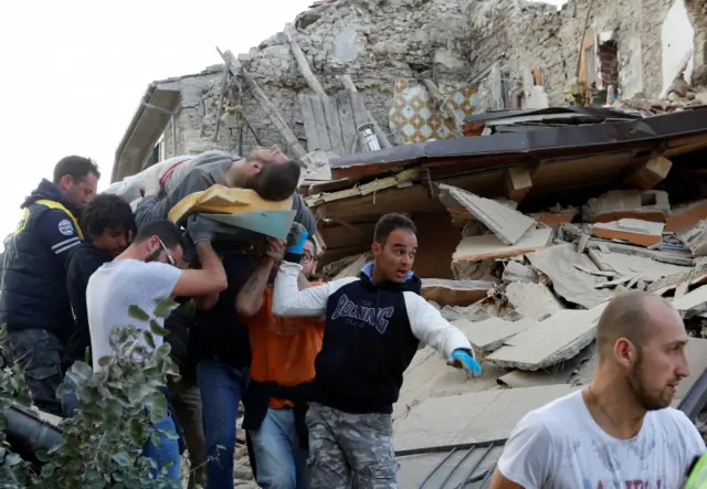 A man is carried away after being rescued alive from the ruins following an earthquake in Amatric