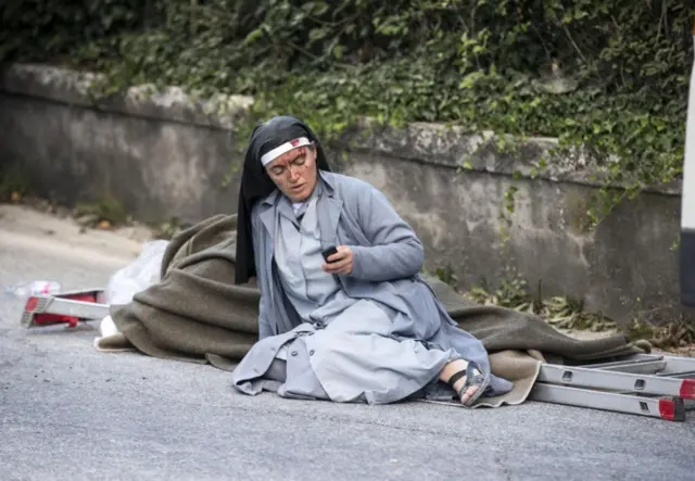 Nun checks her mobile phone in the aftermath of the quake in Amatrice