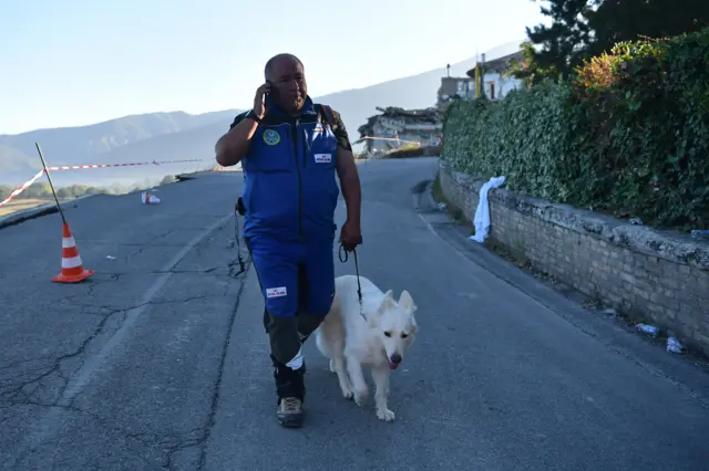 A search dog handler talks on his phone, on August 25, 2016 in Amatrice, Italy.