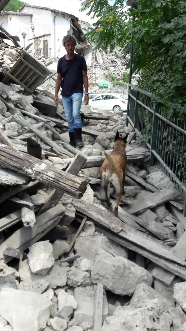 A man in wellyboots and a dog, on a pile of rubble