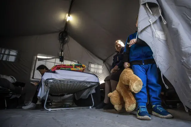 A child holds a stuffed toy as other people sit in a tent set up following Wednesday's earthquake, in Amatrice, central Italy (25 August 2016)