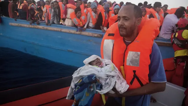 A man carries his five-day-old son after been rescued from a crowded wooden boat as they were fleeing Libya, during a rescue operation at the Mediterranean sea, about 13 miles north of Sabratha, Libya, Monday 29 August 2016.