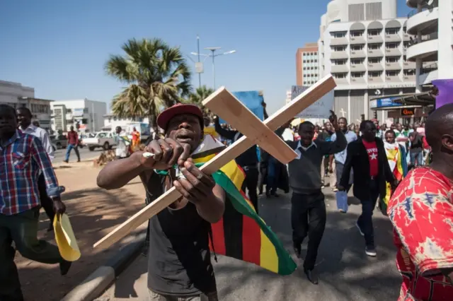 A man, holding a cross, tears a $1,000,000 note bearers" cheques during a protest by several hundred demonstrators gathered in Harare in a fresh outbreak of opposition to President Robert Mugabe, on August 3, 2016.