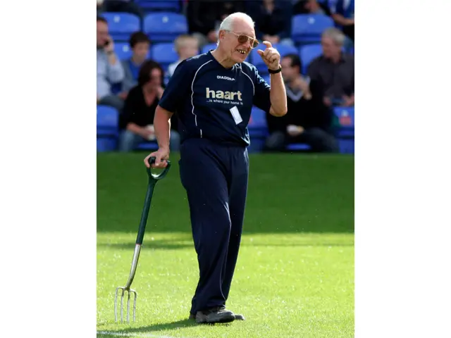 Derek Poole stands on the football pitch holding a garden fork