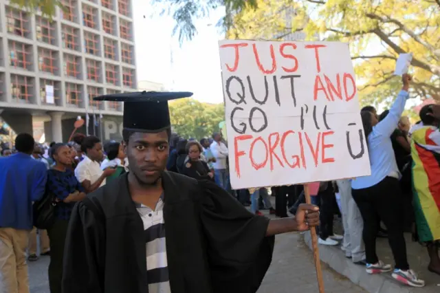 A jobless university graduate poses for a photo while holding a banner with a message directed at Zimbabwean President Robert Mugabe during protests in Harare Wednesday, Aug. 3, 2016