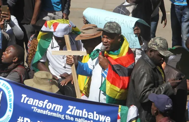 A man prays while holding a cross before demonstrations in Harare, Wednesday, Aug. 3, 2016