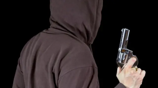 Man wearing hood carrying gun