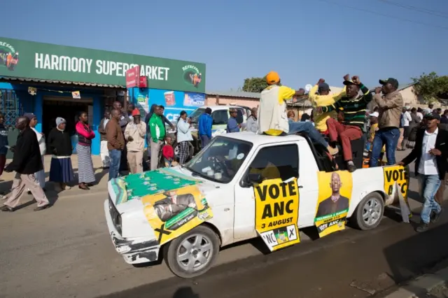 An ANC party vehicle appeals for votes as locals are seen outside a voting station during the Local Government elections in Diepsloot township, north of Johannesburg, South Africa. August 3,2016