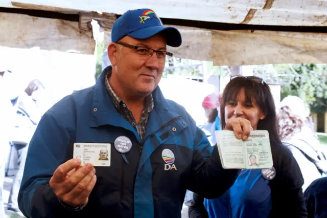 South African main opposition party Democratic Alliance Nelson Mandela Bay mayoral candidate Athol Trollip (C) shows his ID prior to vote in the municipal election at a polling station on August 3, 2016 in Port Elizabeth