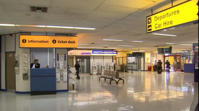 Interior view of Norwich Airport, showing information desk, several passengers, seating and signs