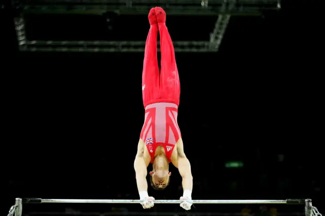 Man Whitlock locked in handstand on horizontal bar