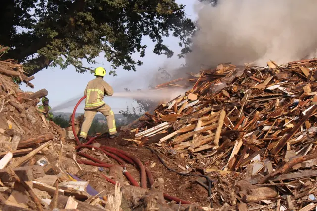 Firefighter uses hose on wood pile fire