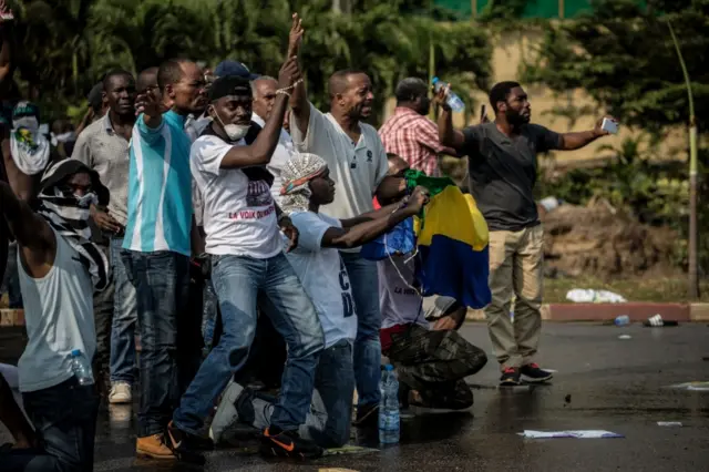 Crowd of Jean Ping supporters gesture towards security forces blocking them from marching