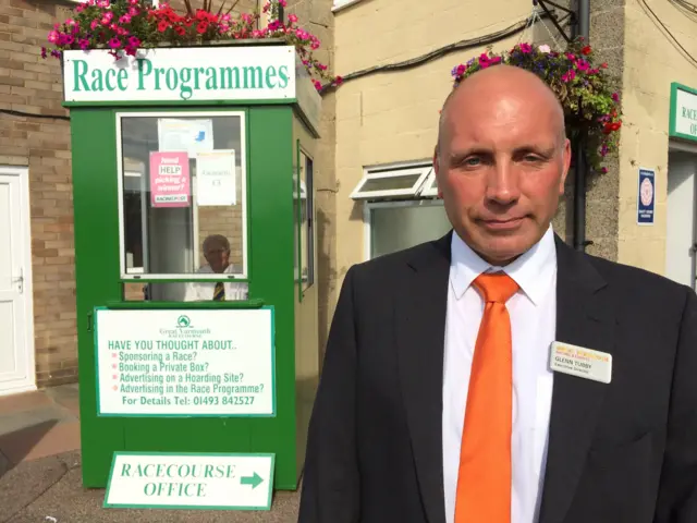 Glenn Tubby at the racecourse, in dark jacket, white shirt and orange tie