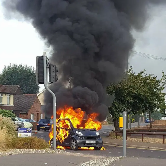 Black Smart vehicle at traffic junction, with flames