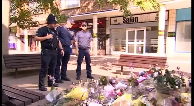 Police officers look at floral tributes