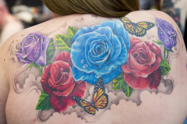 Purple, red and blue roses - with butterflies - tattooed on a woman's back