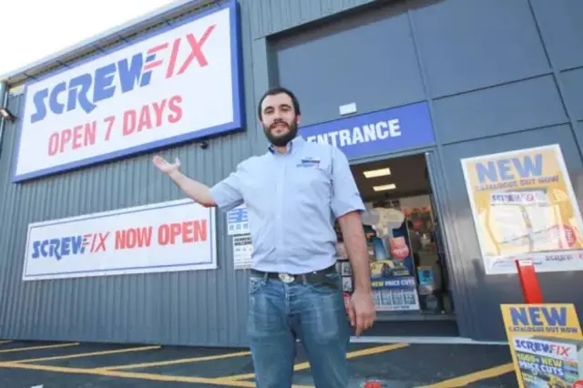 Manager Aristos Yianni, in blue shirt and blue jeans, outside the entrance to his new Screwfix store