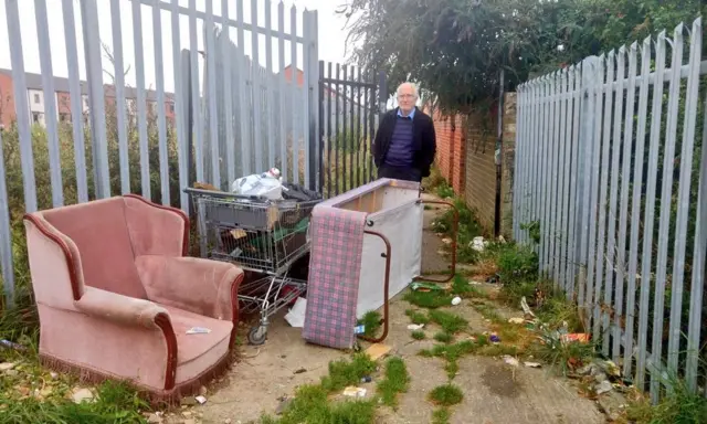 A dumped armchair, bed and trolley full of bags