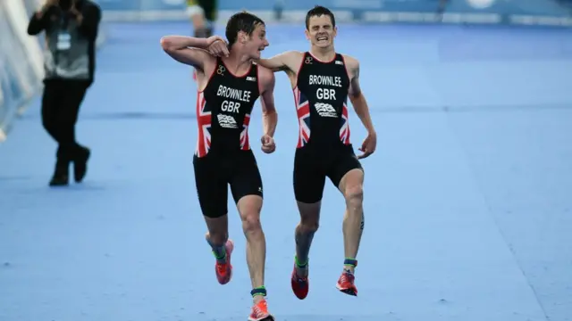 Alistair Brownlee helps his brother Jonathan towards the finish line