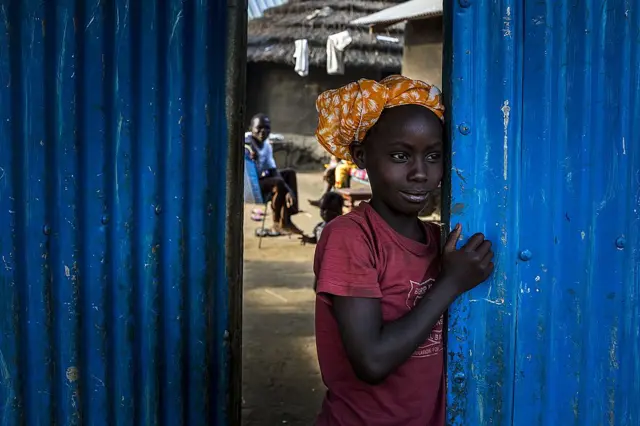 A smiling child standing at an open doorway in Juba, South Sudan