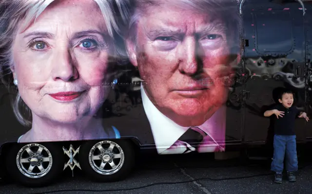 A boy gestures next to a backdrop of US Democratic presidential nominee Hillary Clinton and her Republican counterpart Donald Trump at the Hofstra University, in Hempstead, New York - 26 September 2016