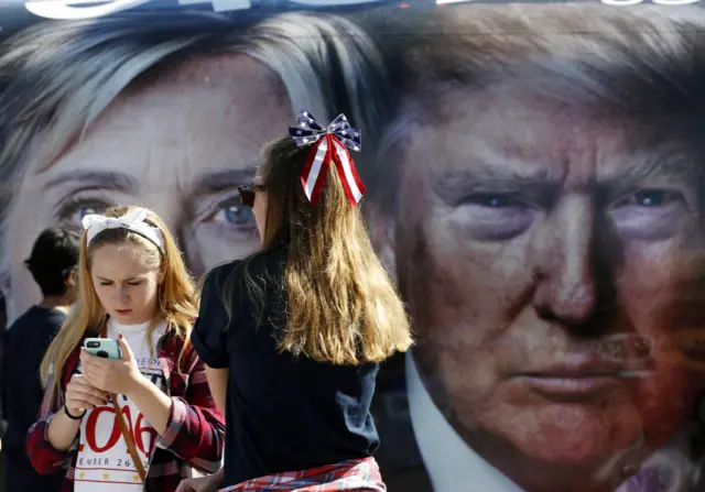 People pause near a bus adorned with large photos of candidates Hillary Clinton and Donald Trump before the presidential debate at Hofstra University in Hempstead, New York.