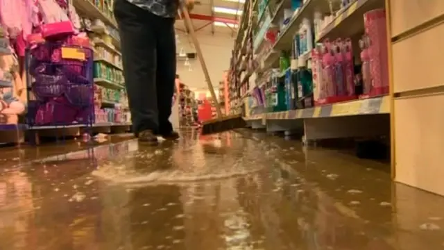 Woman sweeping flood water out from her shop