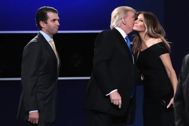 Donald Trump (C) kisses his wife, Melania Trump, while son, Donald Trump, Jr (L) looks on