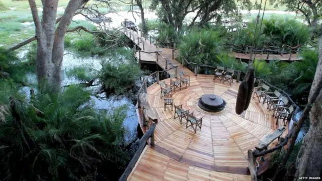 Fancy safari lodge with round wooden seating area and a footbridge