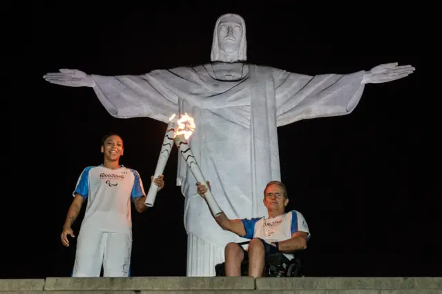 Paralympic and Olympic torchbearers stand in front of the Christ the Redeemer statue in Rio