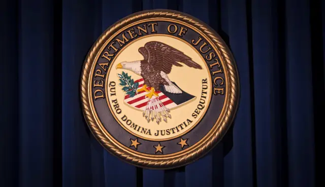 The department of justice logo - a disc with the name on the upper circumference, showing an American eagle clutching a quiver of arrows and an olive branch, perched on a shield in the US colours.