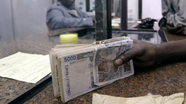 Illustration: A man holds a wad of CFA banknotes