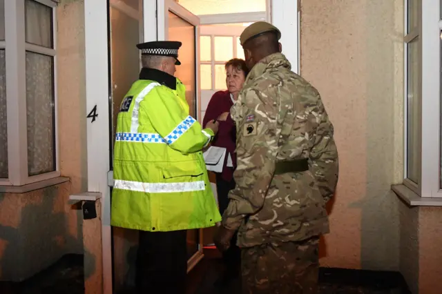 A police officer and army officer warn a resident about flooding