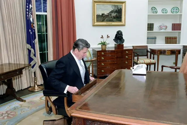 Ronald Reagan sitting at his desk in the Oval Office after assuming office in January 1981