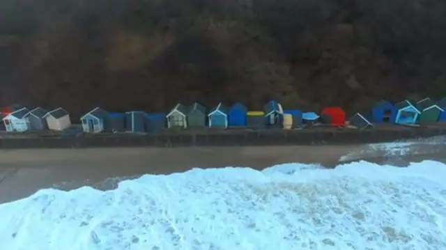 Aerial view of a row of beach huts, some damaged