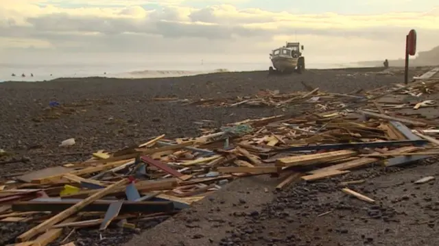 Debris along the beach, with fishing boat in background