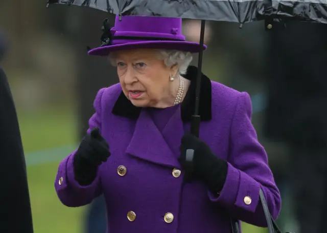 The Queen, in purple coat and hat, holding a black umbrella, at Flitcham church