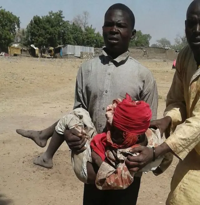 Two men helping a child injured after a camp was bombed in Rann, north-eastern Nigeria