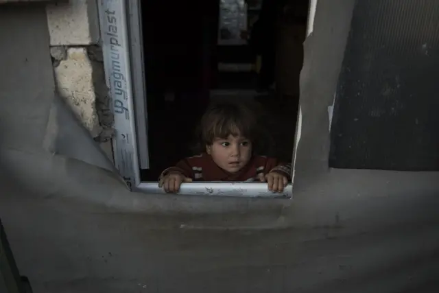 Child looking through a window of a makeshift house in Syria