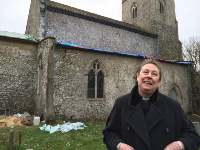 Revd Judith Pollard standing ni front of the church, which has sheeting covering the damaged roof