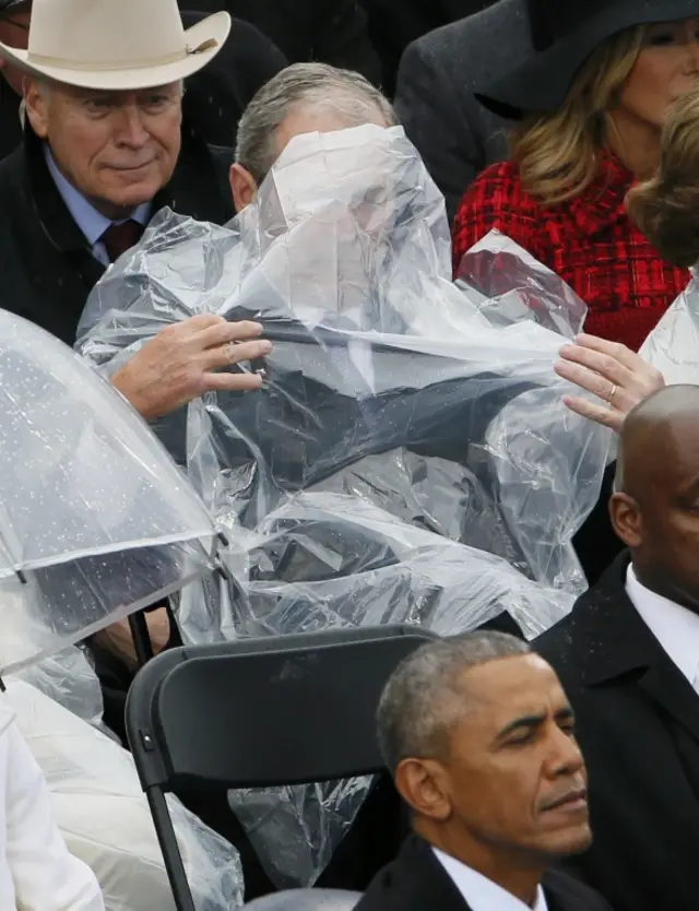 George W Bush struggles with his rain poncho