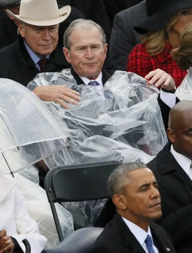 Former US President George W Bush tries to put on his rain poncho