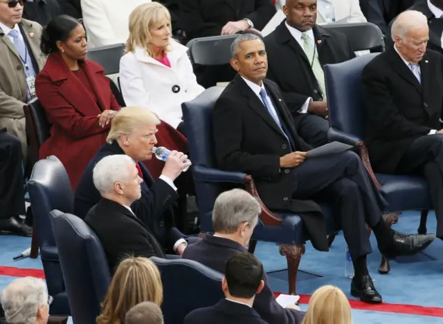 Barack Obama (centre-right) looks over at Donald Trump (centre-left) who takes a drink of water before getting up to take the oath