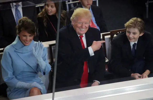 President Donald Trump points to his son Barron while watching the inaugural parade with First Lady Melania Trump