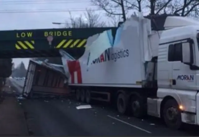 Lorry with shredded trailer stuck under railway bridge